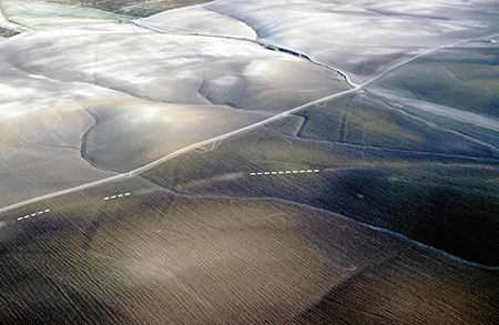 Vista aérea oblicua hacia el sur con las huellas de la vía Augusta que, tras franquear el antiguo estero de (H)asta y Nabrissa (marisma de las Mesas) se incurva hacia el norte para pasar al oeste del cortijo de Espartinas (fotografía L. Ménanteau, 25-11-1978).